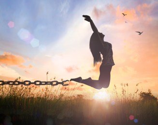 World mental health day concept: Silhouette of a woman jumping and broken chains at orange meadow autumn sunset  with her hands raised